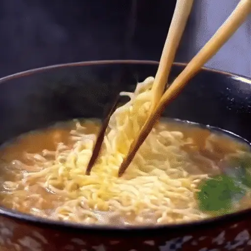 close-up of chopsticks lifting noodles from a steaming bowl of ramen, steam rising
